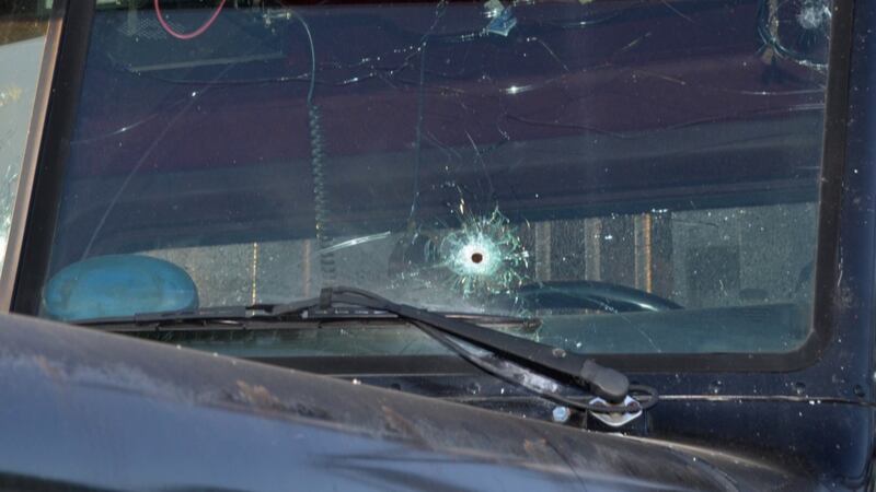 An up-close photograph of the windshield of an 18-wheel logging truck with a large bullet hole...